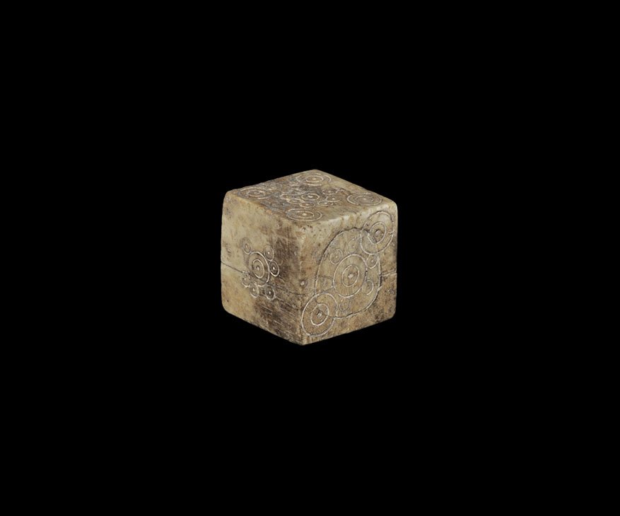 Roman Large Dice: 1st-3rd century AD. A bone cuboid with ring-and-dot spots arranged 6:1, 2:5, 3:4, the central spot to the 1, 3 and 5 with smaller satellite rings; holes to two surfaces plugged. 12 grams, 20mm (3/4").