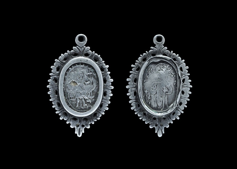 Post Medieval Spanish Reliquary Pendant with Christ and: 17th century AD. A silver reliquary with openwork border and loop above, discoid cell with repoussé images of Christ nimbate in a landscape with staff and scroll, and to the reverse a nimbate ecclesi