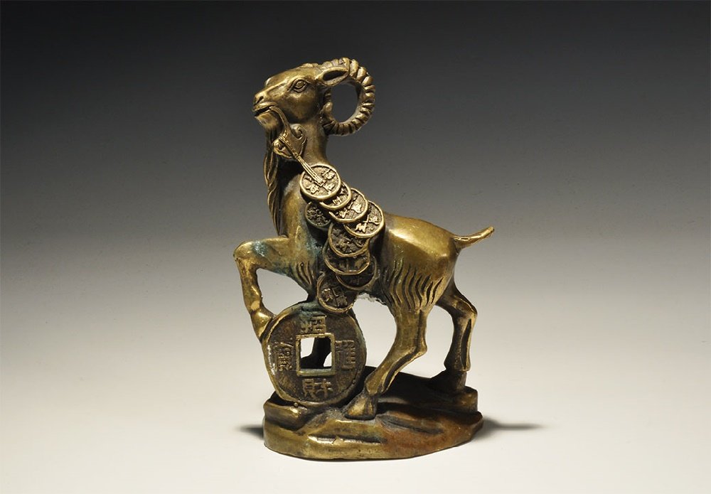 Chinese Style Mouflon Amuletic Figurine: 20th century AD. A bronze figurine of a mouflon sheep on a rocky base, one foreleg resting on a large coin, a lingzhi fungus in the mouth and string of pendant coins; hollow to the underside. 530 gram