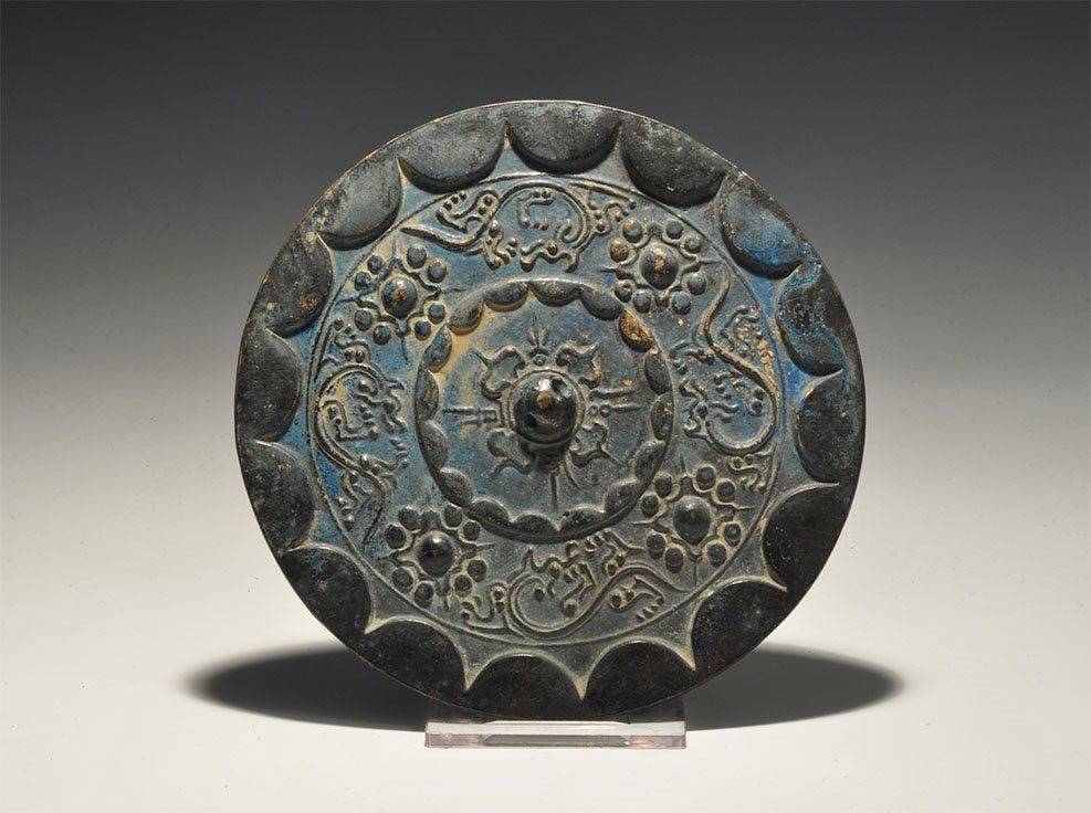 Chinese Style Mirror with Rosettes: An undated archaistic bronze discoid mirror with one polished face, raised rim, central pierced lug, concentric bands of rosettes and tendrils. 385 grams, 14cm (5 1/2"). Acquired on the London art mar