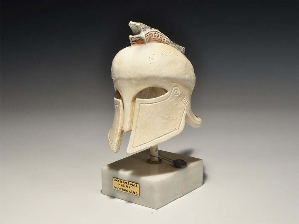 Greek Style Helmet on Base: 20th century AD. A ceramic Corinthian style helmet on a base with pointillé inscription '???????' (Marathon), plaque to the base with mixed Greek and English text. 746 grams, 19cm (7 1/2"). Property 