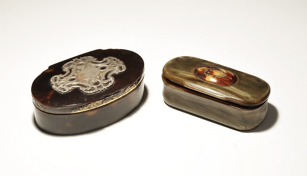 Post Medieval Snuff Box Pair: 19th-20th century AD. A pair of tortoiseshell lidded boxes comprising: a squat mottled brown case with white metal plaque and scrolled openwork surround; a long grey-green container with lip to the fo