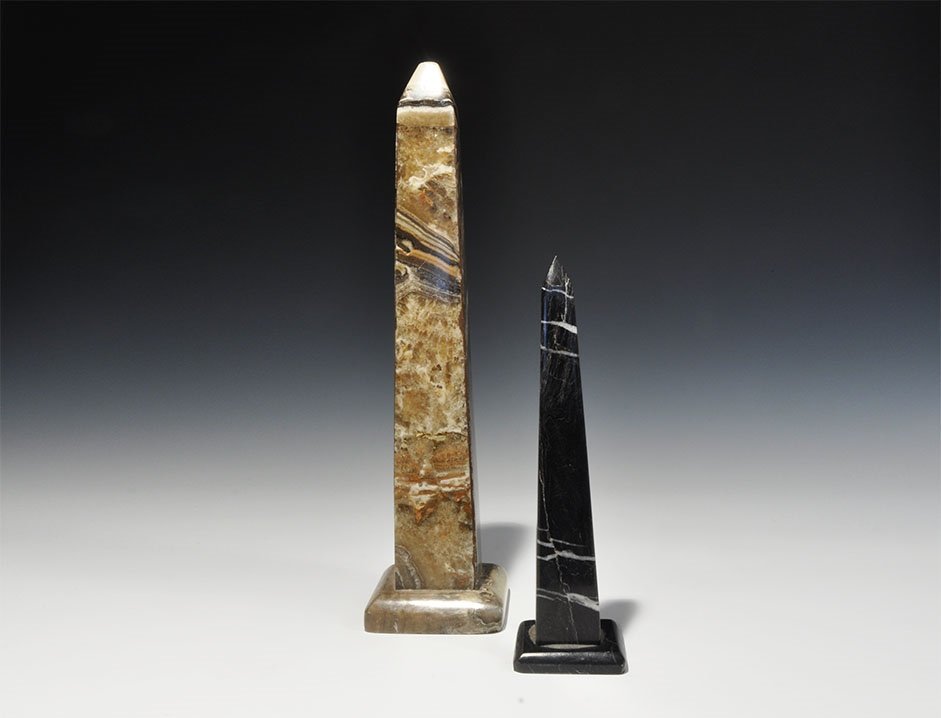 Egyptian Obelisk Pair: 20th century AD. A pair of polished stone obelisks comprising: one in black on low base; one hollow with hole to the base suitable for insertion of a lamp bulb. 1.7 kg total, 22.5-34.5cm (9 - 13 1/2")