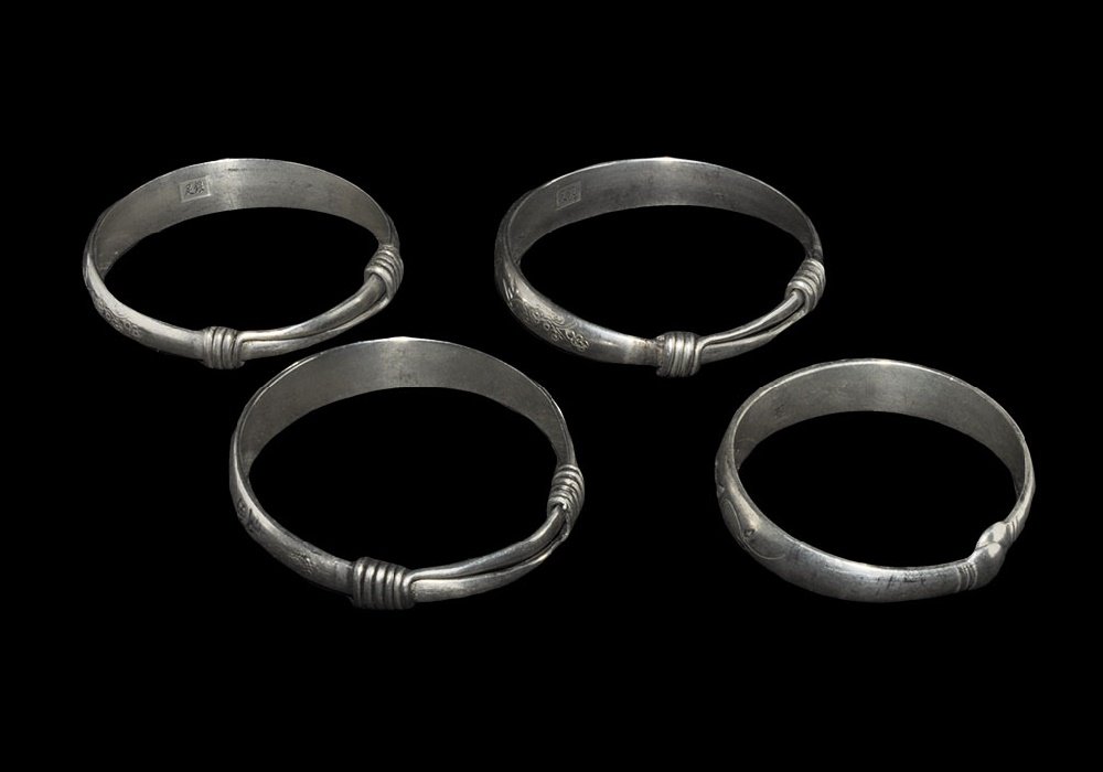 Chinese Style Bracelet Group: 20th century AD. A mixed group of silver coloured metal bracelets comprising: one penannular with incised text; three with incised text and flowers. 150 grams total, 61-70mm (2 1/2 - 2 3/4"). From a c