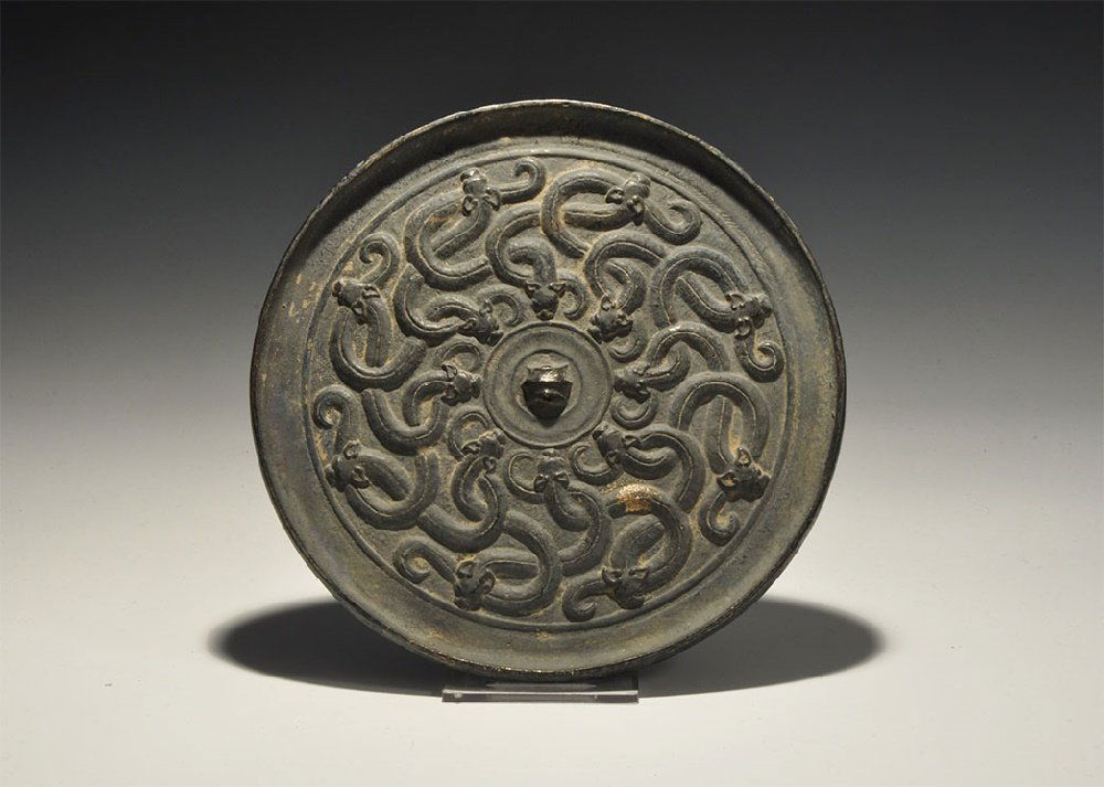 Chinese Style Mirror with Serpents: An undated archaistic bronze discoid mirror with one polished face, raised rim, central pierced lug, mesh of scrolled serpents. 764 grams, 17.5cm (6 3/4"). Property of a London gentleman; acquired bef