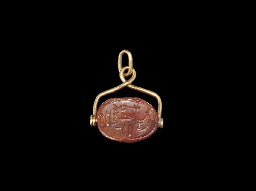 Egyptian Carnelian Queen Nefertari Scarab: New Kingdom, 1550-1077 BC. A carnelian scarab with inscription to the underside of Queen Nefertari (died circa 1250 BC); mounted in a 19th century gold swivel frame pendant. 6.47 grams, 34mm (1 1/2").