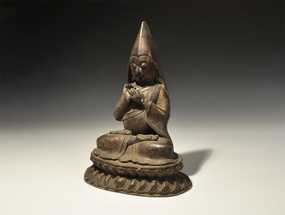 Chinese Large Buddhist Teacher Figurine: 19th century AD. A bronze figure of the Buddhist teacher Tsongkhapa seated on a lotus flower and wearing monastic robes and hat, hands held in front in the teaching pose. 1.81 kg, 30.5cm (12"). Proper