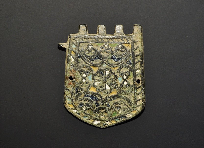 Medieval Enamelled Strap End: 16th century AD. A D-shaped bronze plaque with flanges to three side and hinge-loops above; the main face with ropework border, central design of rosettes and loops, blue, white and yellow enamel; pie