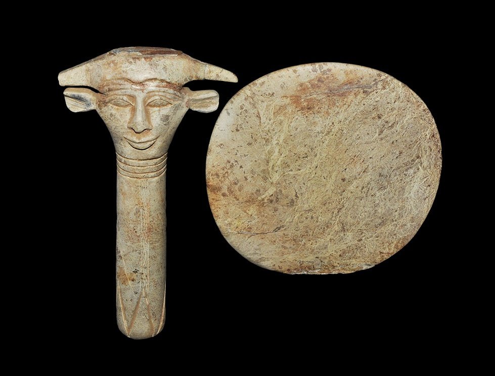Egyptian Style 'Mirror': 20th century AD. A carved rhyolite discoid plaque and waisted columnar handle carved with a row of chevrons at the base, circumferential ribs and face at the junction with fin ears. 468 grams total, 2