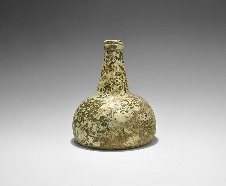 Post Medieval Wine Onion Bottle: 17th century AD. A dark green bell-shaped bottle with pontil base and tapering neck, iridescent surface, flange to the rim. Property of an American gentleman; acquired on the London art market in the 