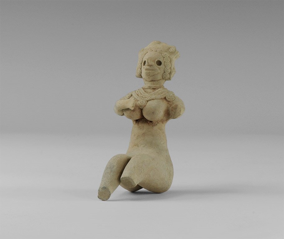 Indus Valley Fertility Idol: 3rd millennium BC. A ceramic figure of a nude female, seated with legs projecting forward and slightly bent at the knees; arms crossed over the breasts, large necklace of three strings with rosette pe