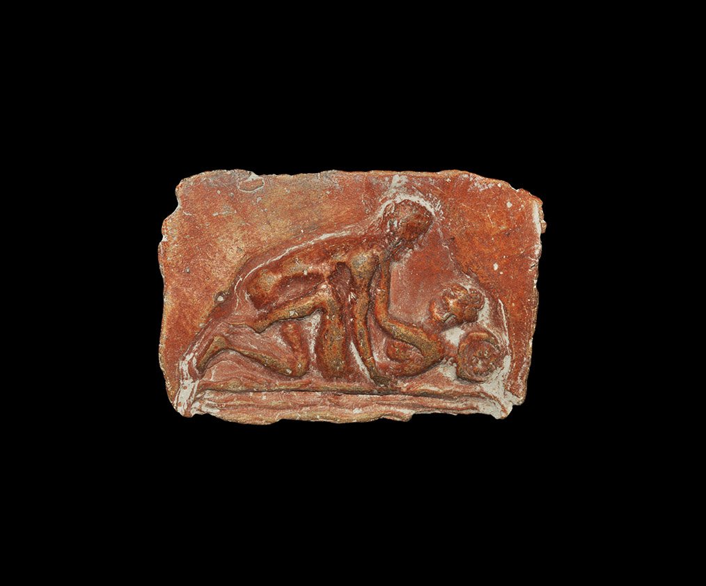 Roman Style Erotic Plaque: . An undated archaistic rectangular terracotta plaque in 1st century BC-2nd century AD style, with erotic scene of two lovers on a couch; mould-formed with the artisan's fingerprints visible on the re