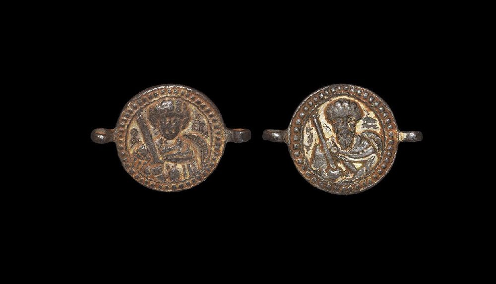Byzantine Gilt Link with Military Saints: 7th-9th century AD. A gilt-bronze link comprising a bifacial discoid plaque with two lateral loops; to one face a youthful male with curly hair, facing holing a sword to his right shoulder, shield to 