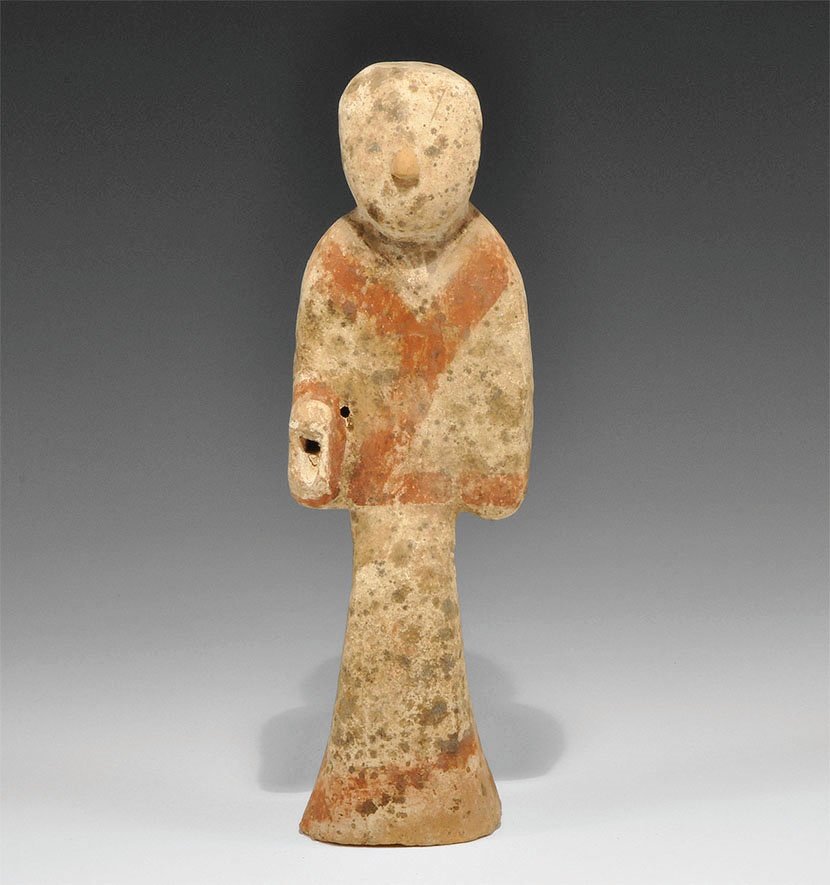 Chinese Attendant Figurine: Han Dynasty, 206 BC-220 AD. A hollow ceramic figurine of a standing attendant in a long coat, the right hand raised; red pigment to the borders of the coat, black pigment to the hair; the hand pierced