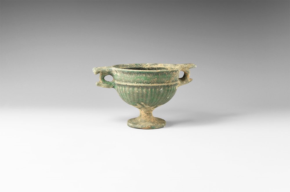 Parthian Footed Skyphos: 1st century BC-1st century AD. A green-glazed ceramic goblet with pedestal foot, hemispherical bowl with ribbed lower body, gusseted band, chamfered rim; two lateral loop handles with projections. 291