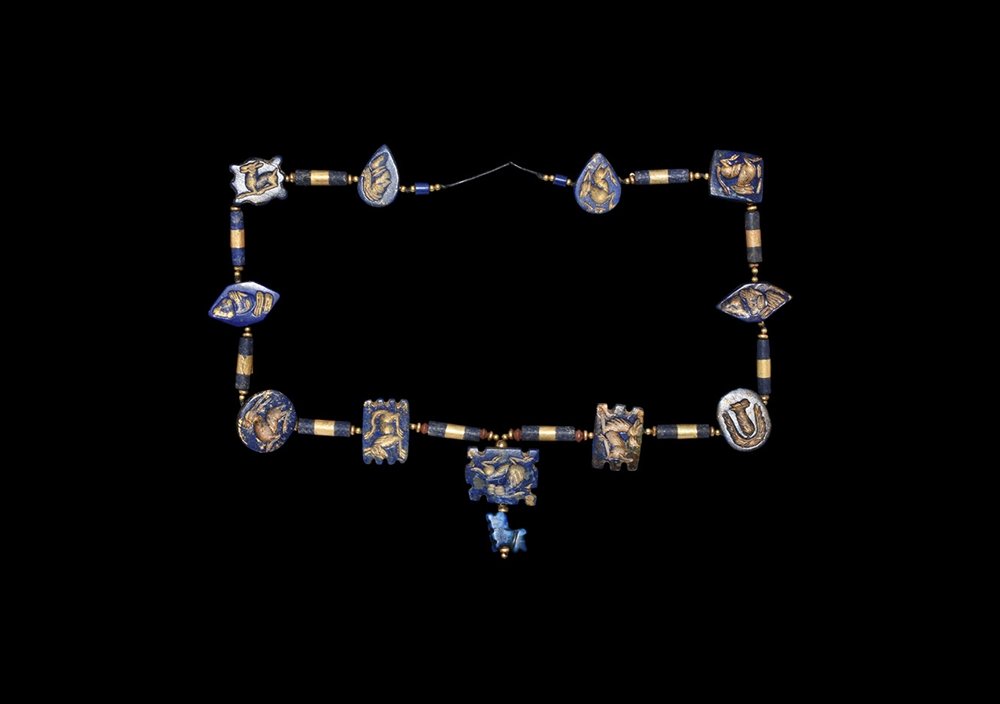 Western Asiatc Gold and 'Lapis' Bead Necklace: 17th-18th century AD. A restrung necklace of lapis lazuli effect glass beads and stamp seals depicting reclining animals and male busts; with gold spacer beads between. 52 grams, 84cm (33"). Acquired 