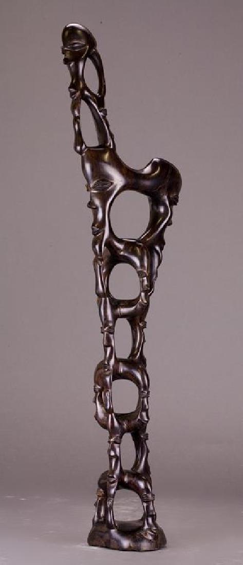 AFRICAN CARVED WOOD SCULPTURE: Structured by stacking rings in which each facet is carved with an human face, rising to a elongated, tall sculpture body. H: 28 in.