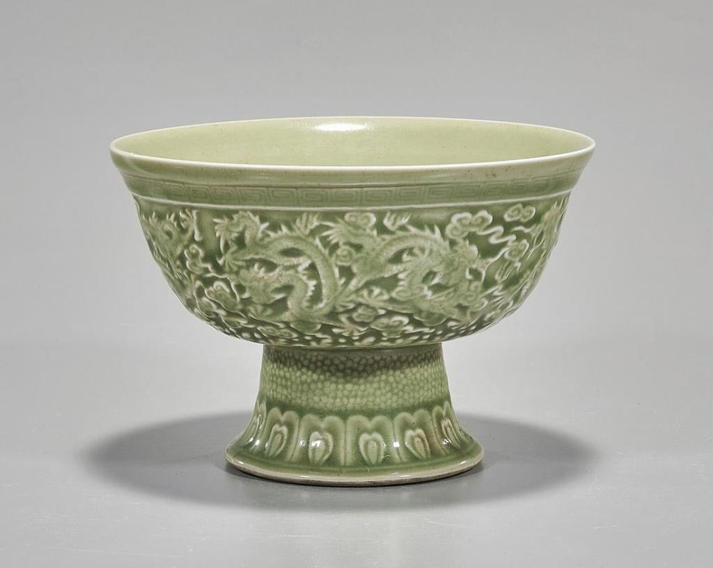 CHINESE CELADON DRAGON STEM BOWL: Of concave form, raised on a tall foot, intricately decorated with dragons in relief around the bowl. Six-character mark in relief on the bottom to read Qianlong. H: 5 in.