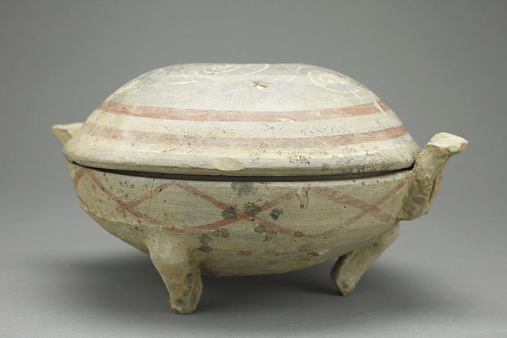 ANTIQUE CHINESE EARTHENWARE TRIPOD LIDDED BOWL: Of a circular form and domed cover, with handles to the sides. The exterior painted with red scroll design. H: 5 1/8 in.