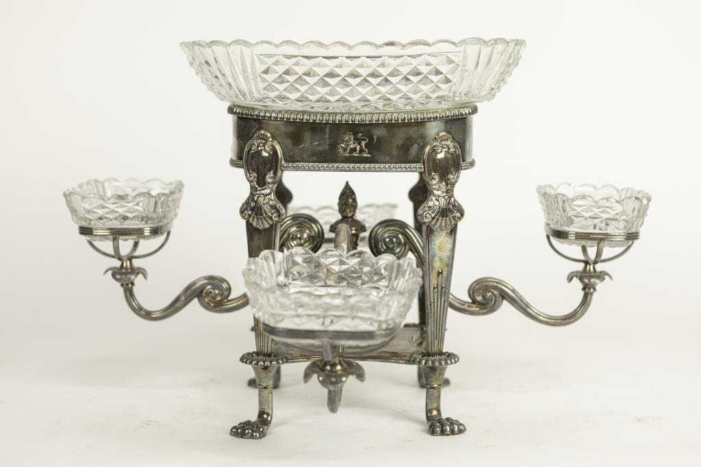 ENGLISH GEORGIAN SILVER-PLATED CENTERPIECE: With a copper-alloy base that is raised on four lion paw legs. Flanked by four detachable, upswept branches on each side in which each holds a smaller glass bowl. Seated with a large matching glass bo