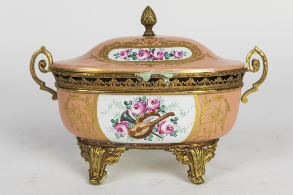 SMALL SEVRES SALMON PINK-GROUND TUREEN: Beautifully hand-painted with blossoming flowers and musical instruments in cartouche, and all around with gilt details, the rim of the dish with gilded rail, and its cover is in matching design. It w