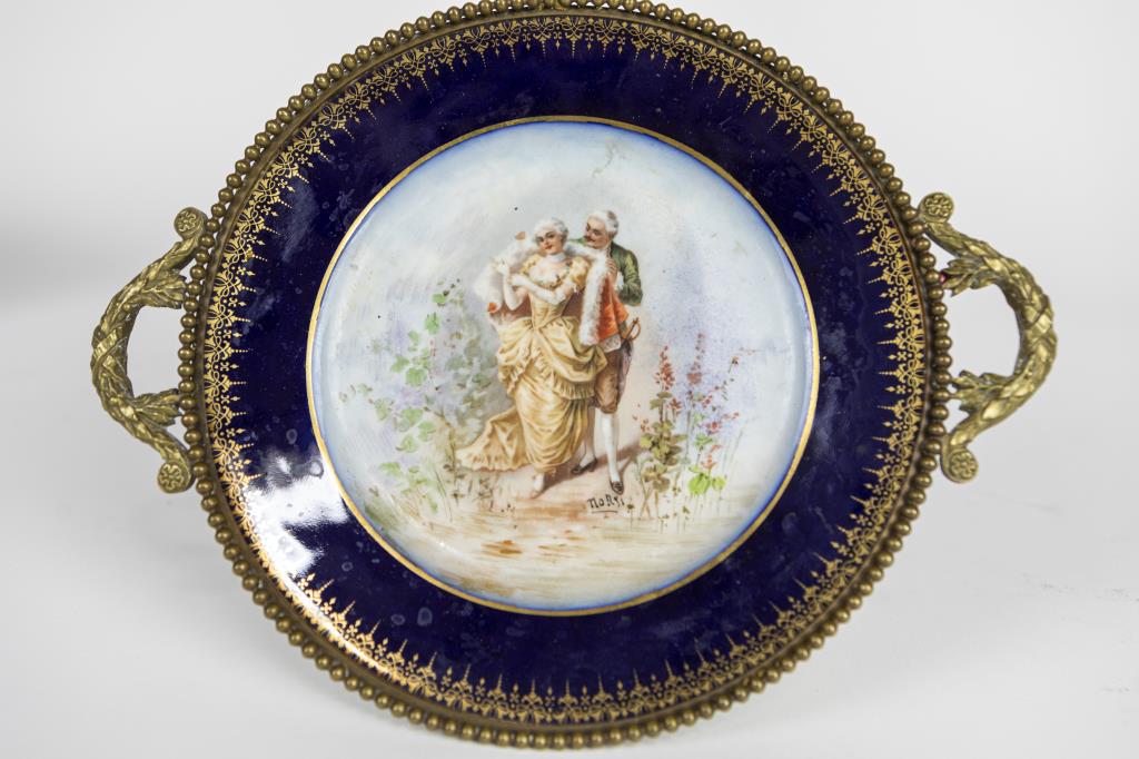 SMALL COBALT BLUE BACKGROUND BONBON DISH: Finely painted with a lover scene in the center of the porcelain dish with gilt details, against a cobalt blue background, the rim with gilt bead rail; signed on lower right to read NORS. Mounted on a