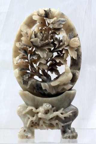A OPEN-WORK SOAPSTONE CARVING OF A GARDEN: H: 10" x L: 5 3/4", detachable by a fitted square soapstone peg from a concave stand with a bulbous body having relief, and standing on four legs