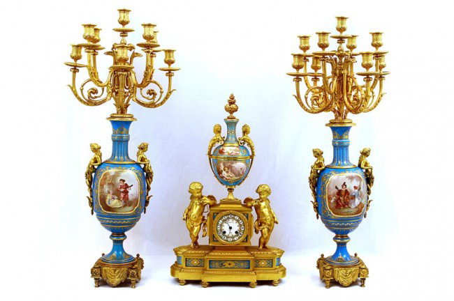TURQUOISE SEVRES PORCELAIN AND ORMOLU CLOCK SET: H: 32" (81cm), 19th century, each nine-branched candelabrum having amorous painting on panel with mounted maidens at either side raised on a square with drapery base; the clock atop with hand-painted