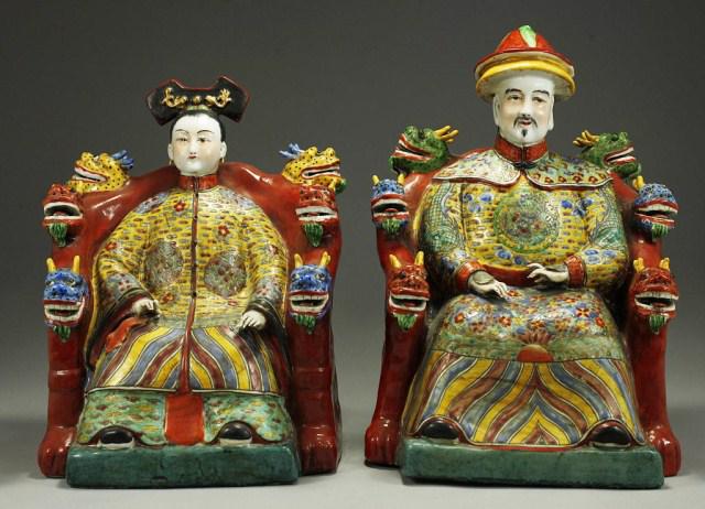 CHINESE PORCELAIN FIGURES OF EMPEROR & EMPRESS: Seated upon red chairs with red, blue and green dragon heads decorating them. The emperor is wearing a red and yellow hat; both empress and the emperor are dressed in royal attire. Republic period. H: