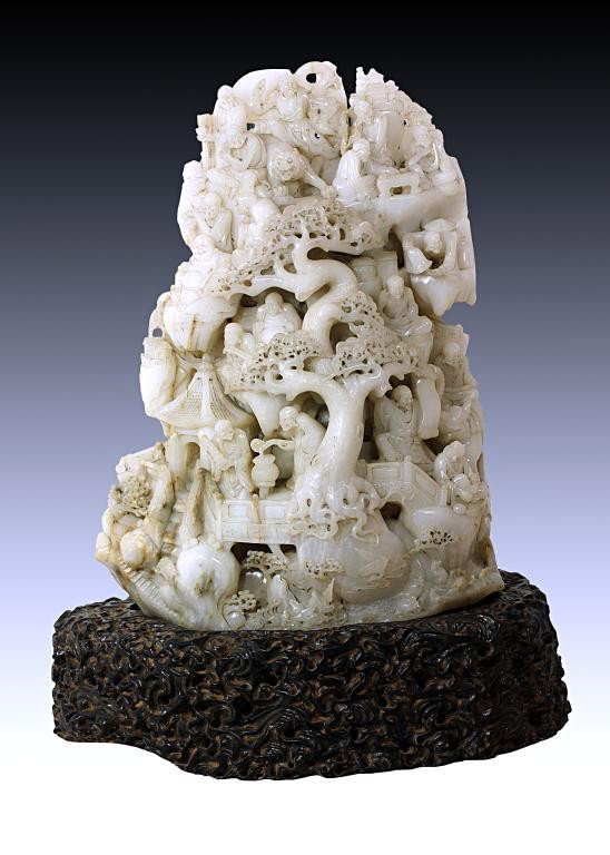 ANTIQUE CHINESE WHITE JADE BOULDER OF 18 LOHANS: If you wish to bid on this lot, please contact the Asian Art Department + 1 310 770 5444. A finely carved large jade depicting of the18 lohans within a temple complex, on a carved fitted oval wooden p