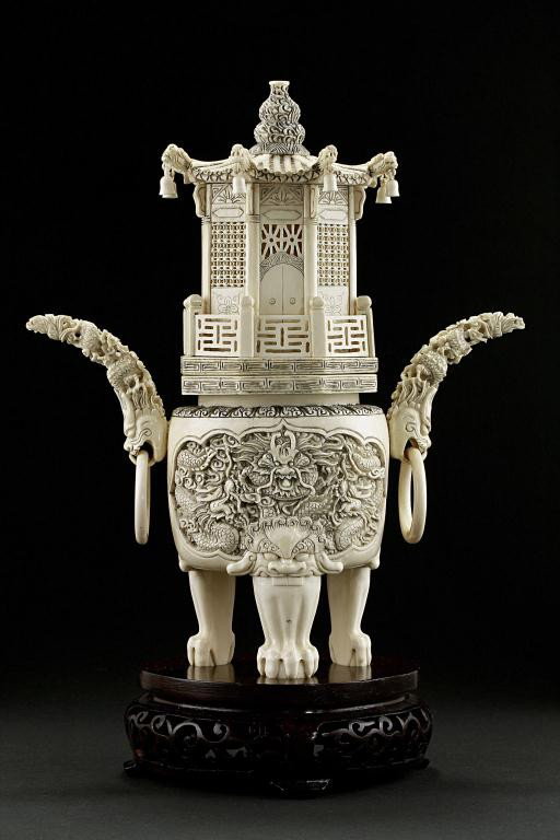 CHINESE CARVED IVORY TRIPOD CENSER WITH COVER: Being supported by three claw on balls stands on a carved wooden base each issuing from head of a beast, the body heavily carved in detail of scaly dragons, while flanked at each sides with a horn-hea