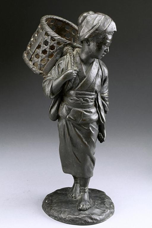 JAPANESE FIGURE OF AN OKIMONO: Metal figure of a geisha carrying a weaved basket on the shoulder, the right hand holding the strap while the left hand holds a stick. H: 11 1/4 in.(28.5cm)