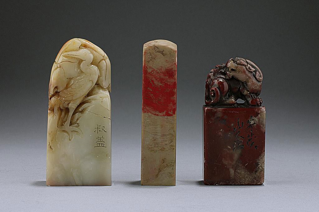 THREE CHINESE CARVED STONE SEAL MARK: One surmounted by a crane perched on rockery, one of a lion with bifurcated tails and its head turned to its body, and the other in obelisk form with red pigment strewn around its upper body. H: 3 1/8