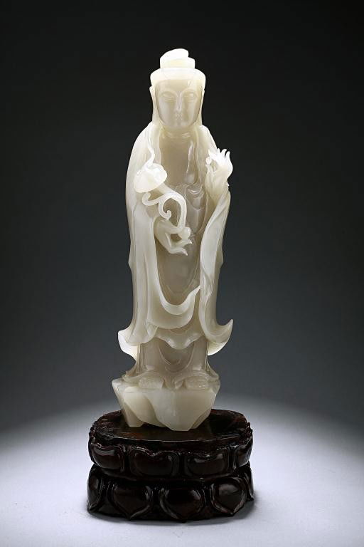 CHINESE CARVED WHITE JADE FIGURE OF A GUANYIN: Delicately carved with the Goddess of Mercy standing in her long flowing robe, and holding a ruyi scepter in her right hand, while her left hand holding a pearl with her thumb and index finger. Set on