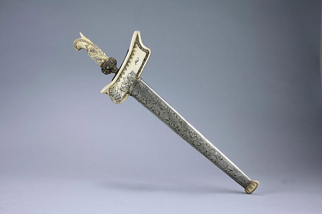 ANTIQUE DECORATIVE INDONESIAN METAL DAGGER: Finely decorated scabbard with walrus ivory chape and locket protects the wavy blade with bejeweled round cross guard and ivory hilt. L: 18 3/8 in.(46.5cm)