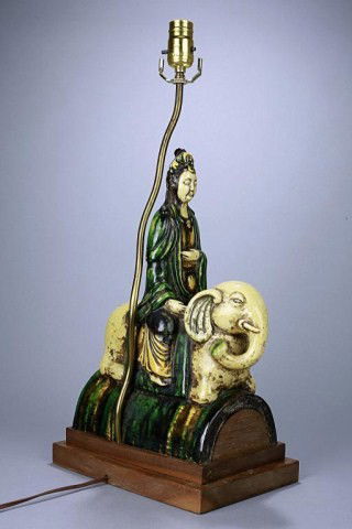CHINESE FIGURE OF A SAMANTABHADRA ATOP AN ELEPHANT: In her voluminous robe in rich green tone rides atop a recumbent elephant on a semi-lune plinth. Heavily glazed in three colors. Used as support base for a lamp. H: 15 1/2 in. (39.5cm)