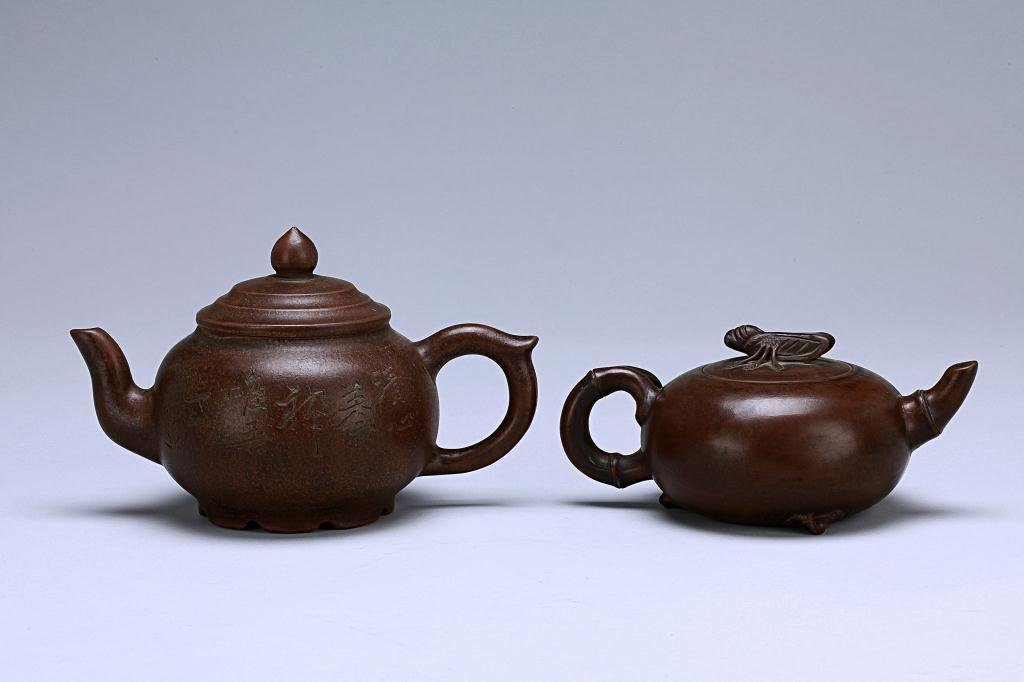 TWO CHINESE TERRA COTTA TEA POTS: Of compressed spherical form rising from a short base, with tiered cover and conical finial, flanked with a leaf-capped loop handle and short spout, the body etched with prunus blossoms and branches, 