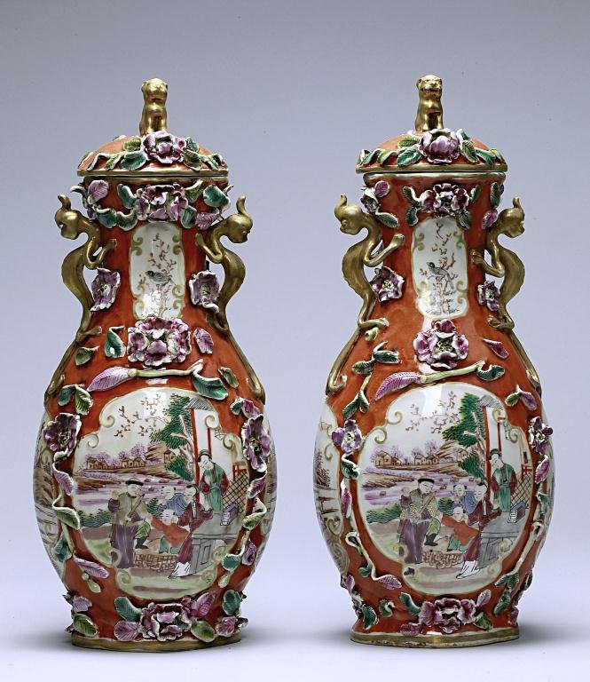 CHINESE FAMILLE ROSE CORAL GROUND VASE WITH COVER: Both of ovoid forms with domed covers with a recumbent qilin knop flanked by two lizards as handles, enameled to the body with two roundels depicting figural scenes and another two panels to the sides