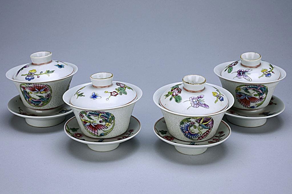 CHINESE FAMILLE ROSE FOUR PORCELAIN TEACUPS: Each delicate tea cup hand painted in vibrant colors with roundels of butterflies amidst spring flowers borne on incised leafy tendrils and scroll, above lotus bloom around the base, the domed covers