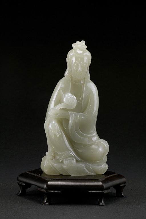 CHINESE WHITE JADE FIGURE OF A GUANYIN: wearing a billowy robe, and holding a scepter, on a hexagonal wooden base. H: 4 5/8 in.(12cm).