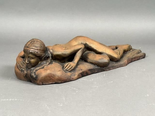 CAST METAL FIGURAL STATUE, OF A RECLINING BEAUTY: Lying naked partially on her stomach, her hair styled in two low ponytails while her head rests on the headrest of a futon. With signature by artist, Robert Blake.H: 4 1/2 in. L: 18 in. W: 7 3/8 in.