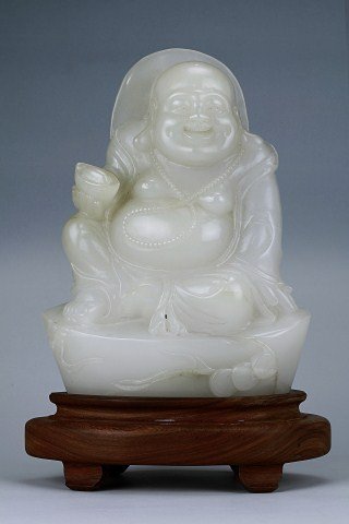 CHINESE NEPHRITE JADE BUDDHA: Avery well carved seated laughing Buddha with a mandorla at the back, wearing a nenju around his neck down to his ample belly and dressed in loose billowy robe with his right hand resting on his raise