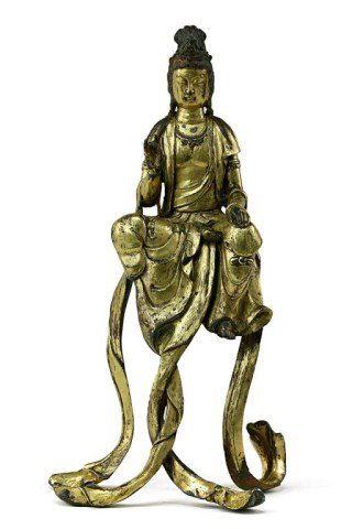 ANTIQUE CHINESE GILT-BRONZE FIGURE, OF A GUANYIN: Well cast seated deity in “Royal ease” position and seemingly floating in the air on sash supports, with the hair set in a tall chignon and the face with serene expression, dressed in long robes a