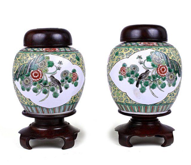 PAIR OF CHINESE PORCELAIN GINGER JARS: 19th Century. Of ovoid forms placed on carved wooden stands, brightly enameled to the body with two quatrefoil reserves depicting a long tailed bird perched on dense floral rockery, and mountainous ri