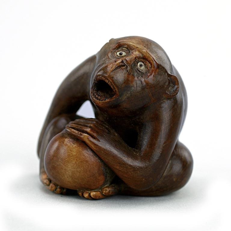 JAPANESE CARVED WOOD NETSUKE FIGURE OF A MONKEY: Well carved figure of a crouching monkey with its mouth opened wide; and with a chestnut placed in between its legs and its left hand placed on top of the nut, while the other on his side; signed at t