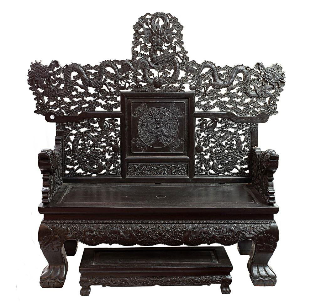 CHINESE CARVED HARD WOOD BENCH: Of rectangular-shaped seat, flanked by an intricately carved writhing dragon amidst scrolling clouds, as armrests; the back support with a central carved medallion of a ferocious dragon in pursuit of