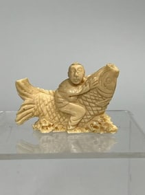 A CARVED STONE OF A FISH BOARDED ATOP BY A BOY