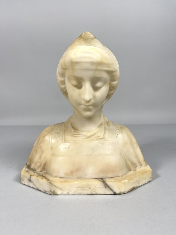 CARVED WHITE MARBLE BUST OF A LADY: Features a serene lady, elegantly poised with a gentle expression that evokes a sense of tranquility. The bust is mounted on a base. H: 9 in. L: 8 1/2 in. W: 4 1/2 in.