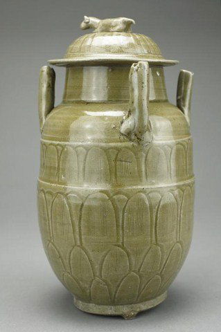 CHINESE EARTHENWARE LIDDED JAR: with four tube handles to the shoulders, possibly five dynasties to early Song. H: 9 3/4 in. The body incised with upright petal leaves, all under a green glaze, the cover surmounted by a dog as finia