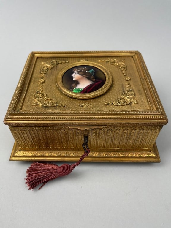 GILT BRONZE JEWELRY BOX, WITH A KEY: Raised on four short legs, and decorated with a painted emblem of a lady portrait. L: 7 in. W: 5 3/4 in.